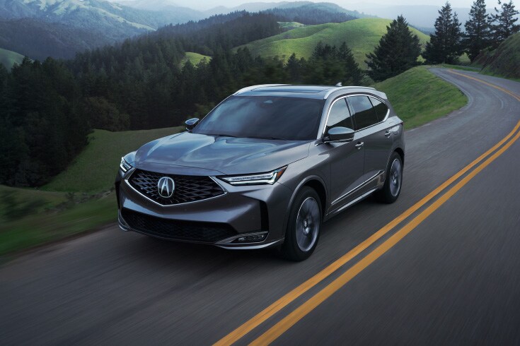 2026 Acura MDX with Advance Package in Liquid Carbon Metallic, driving on the road in a three-quarter view (Premium Performance SUV). 2026 Acura MDX with Advance Package in Liquid Carbon Metallic, driving on the road in a three-quarter view (Premium Performance SUV).